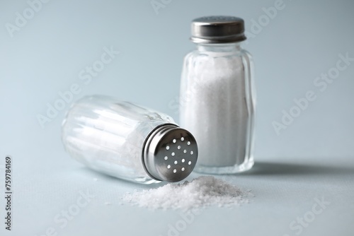 Natural salt in shakers on color background