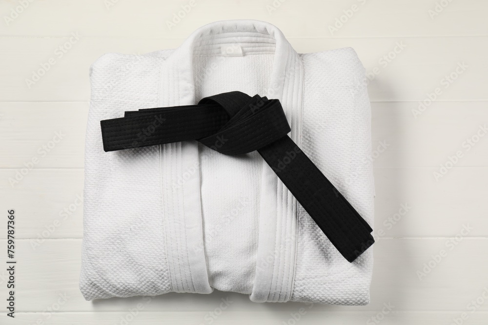 Naklejka premium Black karate belt and white kimono on wooden background, top view