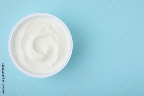 Delicious natural yogurt in plastic cup on light blue background, top view. Space for text