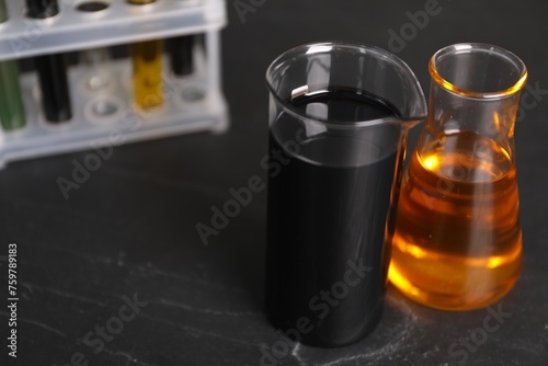 Beaker and flask with different types of oil on grey textured table, closeup. Space for text