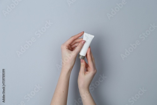 Woman holding tube of cream on grey background, closeup