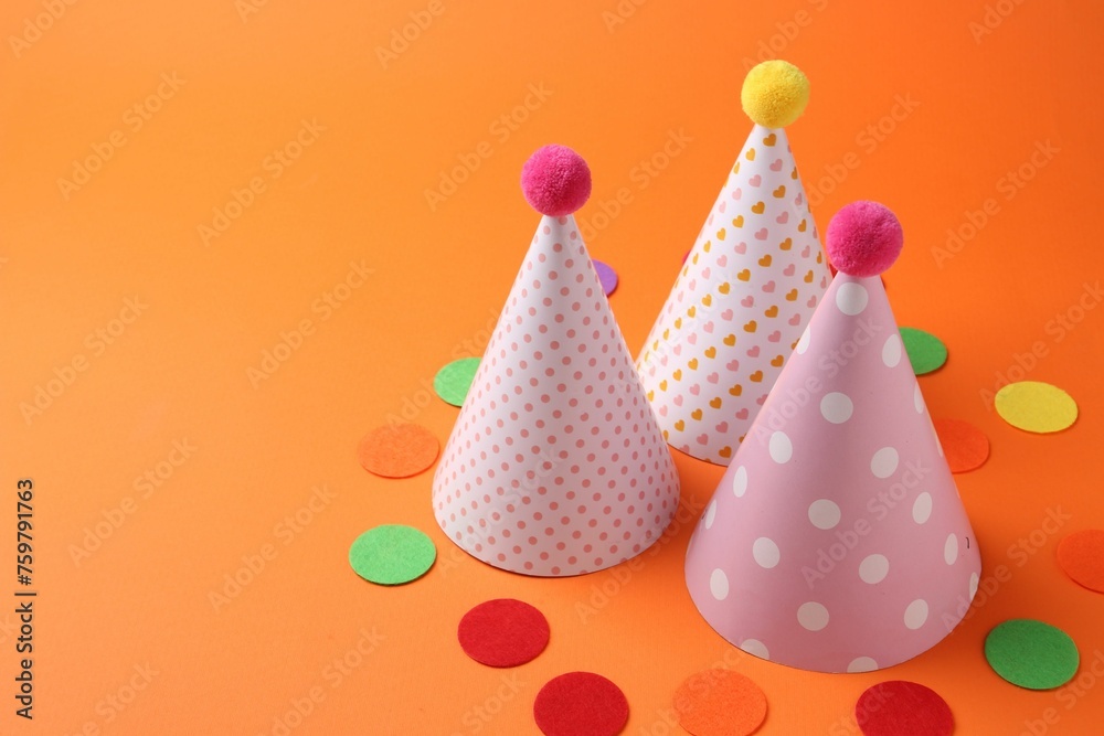 Party hats and colorful confetti on orange background. Space for text
