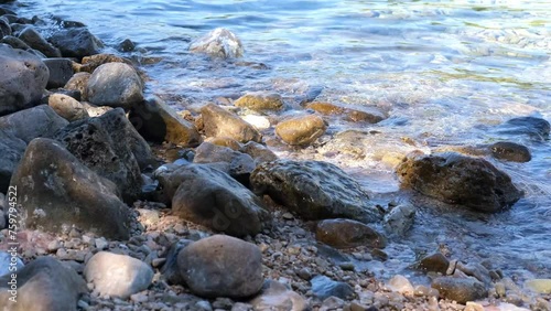 Clear and transparent blue sea water glistens and shimmers in the sun and washes large coastal stones. The concept of tourism, seaside summer holidays, copy space photo