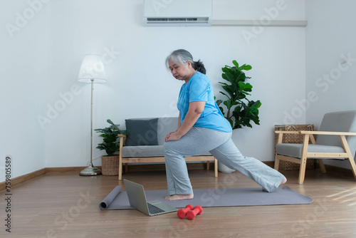 Asian elderly woman exercising at home by stretching her leg muscles and using dumbbells as an exercise aid for retirement people and health care concept.