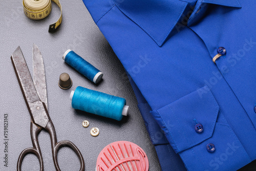 Two folded blue long-sleeved shirts, thread, scissors and other tools for minor repairs of household clothes