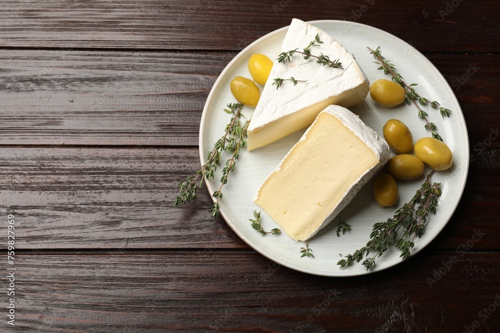 Plate with pieces of tasty camembert cheese, olives and rosemary on wooden table, top view. Space for text