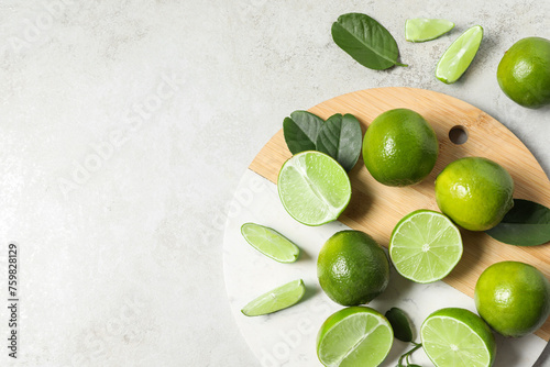 Fresh ripe limes and leaves on light table, top view. Space for text