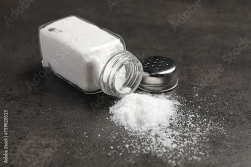 Overturned shaker with salt on grey table photo