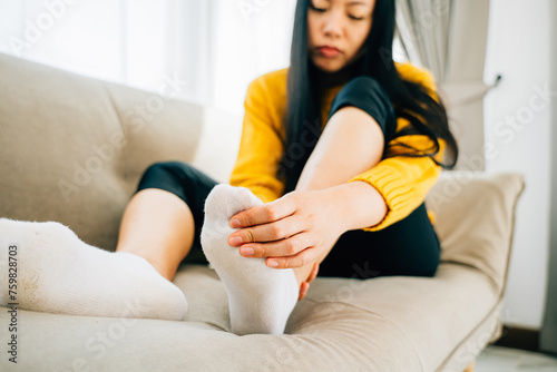 Depicting health care concept, a woman sitting on a sofa massaging her painful foot with a highlighted area indicating pain. Emphasizing recovery reflexology and relief from discomfort. photo