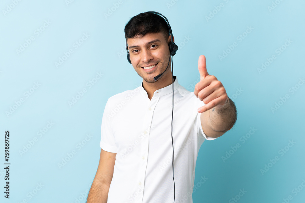Telemarketer Colombian man working with a headset over isolated background with thumbs up because something good has happened