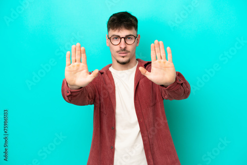 Young caucasian handsome man isolated on blue background making stop gesture and disappointed