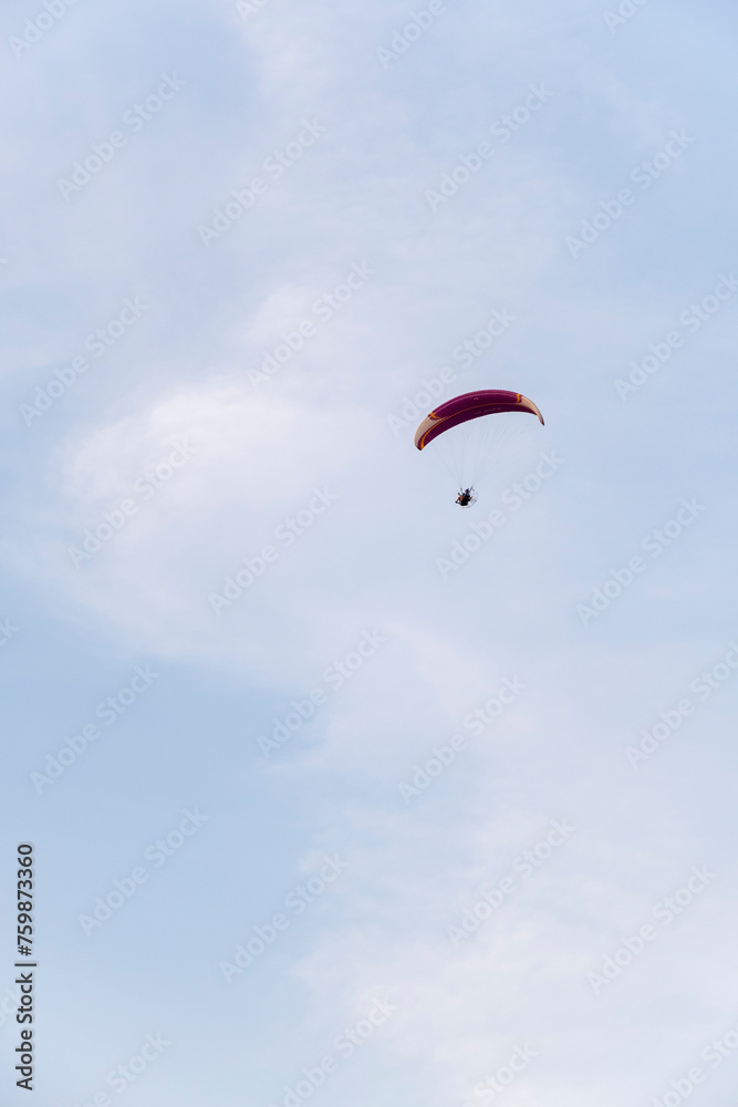 A paraglider or paramotor flying over a beautiful blue sky with white clouds over the beach.Real Photo A paraglider or paramotor flying over a beautiful blue sky with white clouds over the beach.Real Photo