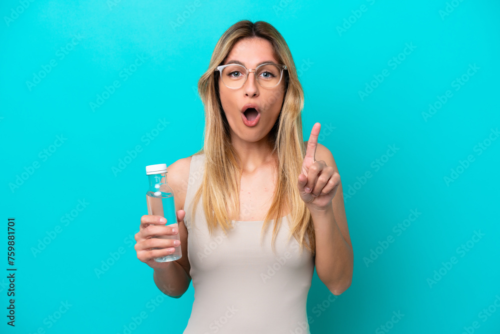 Young Uruguayan woman with a bottle of water isolated on blue background intending to realizes the solution while lifting a finger up Young Uruguayan woman with a bottle of water isolated on blue background intending to realizes the solution while lifting a finger up