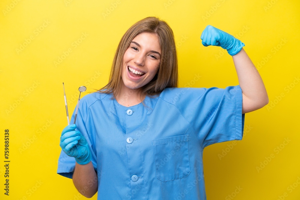 Dentist caucasian woman holding tools isolated on yellow background doing strong gesture Dentist caucasian woman holding tools isolated on yellow background doing strong gesture