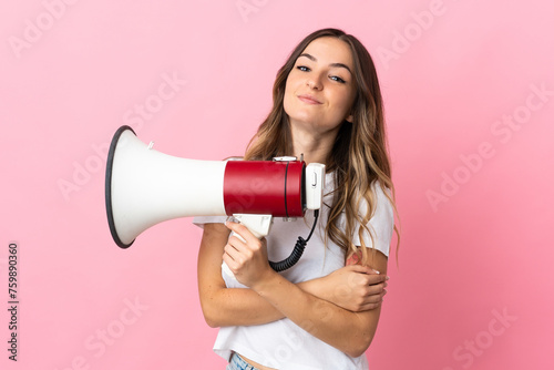 Young Romanian woman isolated on pink background holding a megaphone and smiling