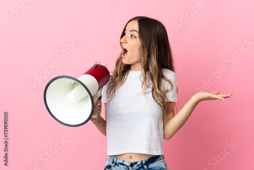 Young Romanian woman isolated on pink background holding a megaphone and with surprise facial expression