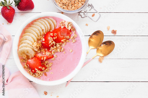Healthy strawberry and banana smoothie bowl with granola. Top down view table scene on a white wood background.