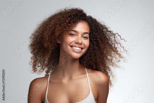 Gorgeous woman with voluminous curly hair and a beaming smile, wearing a white tank top