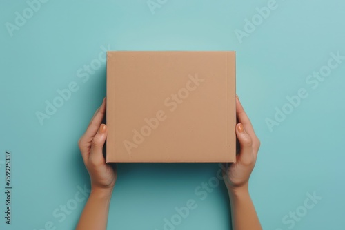 A person standing against a blue background, holding a brown box in their hands.