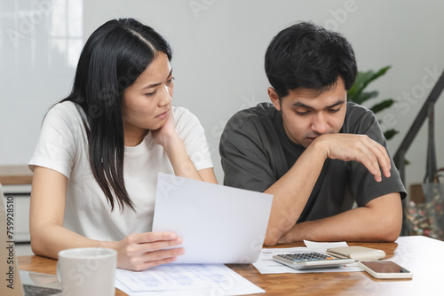 Stressed Asian couple looking at financial debt notice papers from bank.