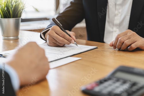 Fototapeta Naklejka Na Ścianę i Meble -  businessman sitting at desk holds pen signing contract paper, lease mortgage, employment hr or affirm partnership