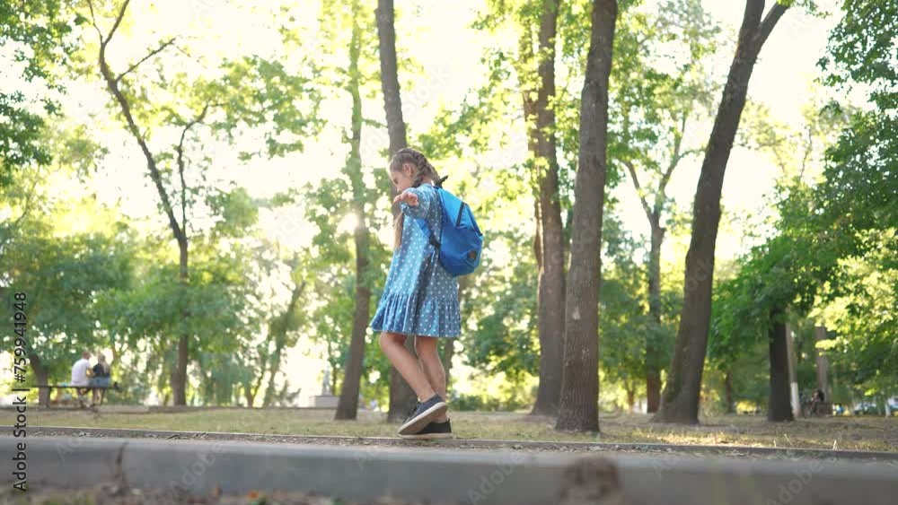 little girl walking along the curb. concept of a happy childhood and loving family. a schoolgirl in a dress and with a blue backpack walks lifestyle along the curb, keeps her balance little girl walking along the curb. concept of a happy childhood and loving family. a schoolgirl in a dress and with a blue backpack walks lifestyle along the curb, keeps her balance