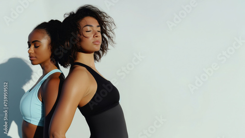 two females back to back, one wearing light blue fitness wear and the second in a black yoga suit against a white background