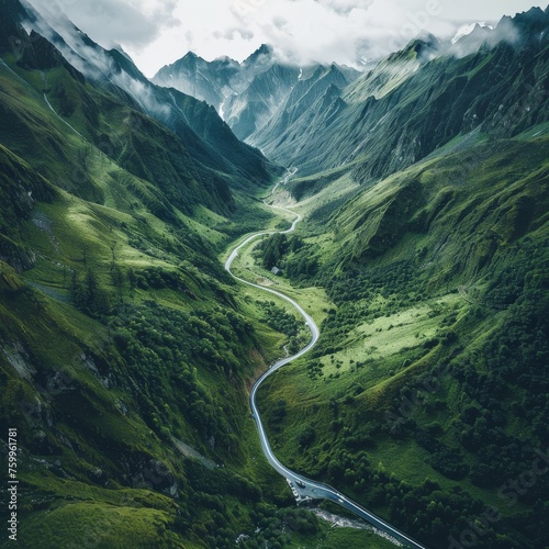 Aerial view of a winding road snaking through a lush green mountainous landscape with misty peaks.
