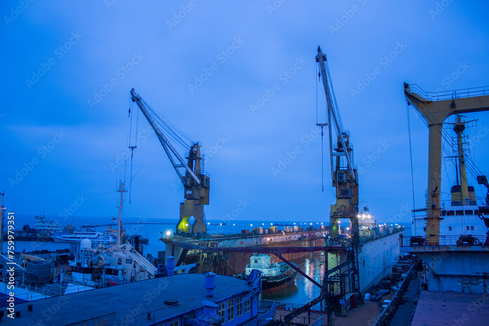 Twilight at shipyard with floating dock, vessels undergoing repair amid towering cranes. Maritime industry, heavy machinery at work, shipping business infrastructure, nautical vessel maintenance.