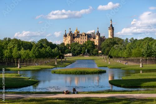 View through the palace gardens towards Schwerin Palace. Reflection in the water. Sunny day with light clouds.