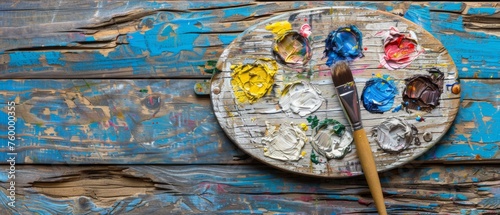  A wooden table holds a palette of paint with a brush at its center, while another brush rests on the palette.