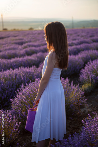 Back view of a young girl poses in a field of lavender flowers at sunset.