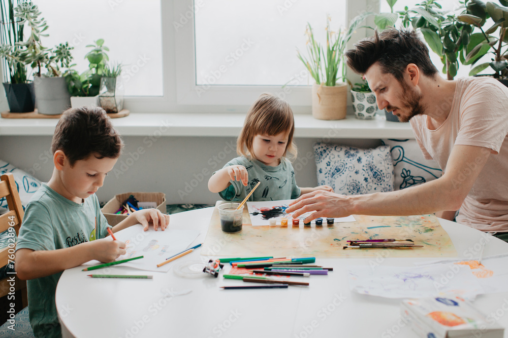 The boy and Little sister with father draws with pencils at the kitchen The boy and Little sister with father draws with pencils at the kitchen