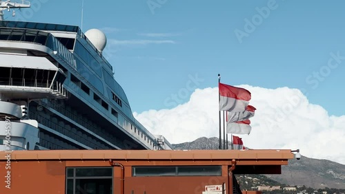 a huge cruise ship stands at the pier, mountains in the background, Flags of principality of Monaco in the wind at sunny weather, the port of Hercules photo
