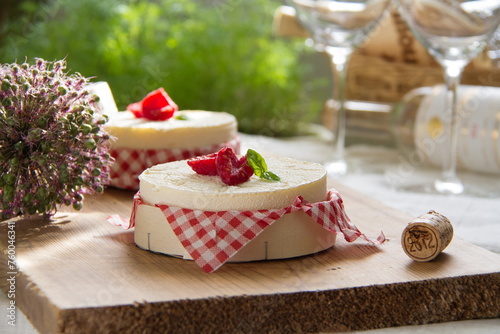 Summer mini cheesecakes with raspberries served on a wooden table, in the background there are glasses and a bottle of wine for a picnic, a romantic date. French mousse cake in the sunlight. Close up © Foodie Studio