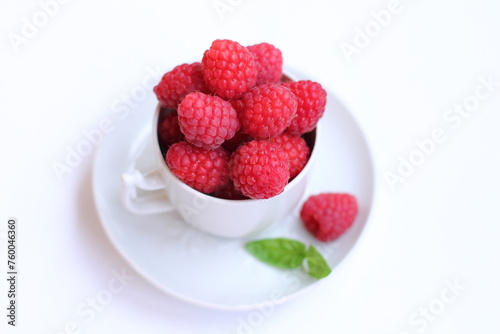 Lots of raspberries in a white rustic cup, green basil leaf on a white background isolated. Fresh ripe summer berries on a plate. Close. up © Foodie Studio