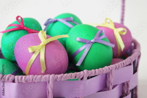 Multi-colored Easter eggs decorated with ribbons in a wicker basket on white background. Family religious traditions © Foodie Studio
