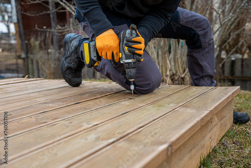 Obraz na płótnie Deck or terrace construction, builder hand with electric screwdriver installing impregnated wooden boards w salonie