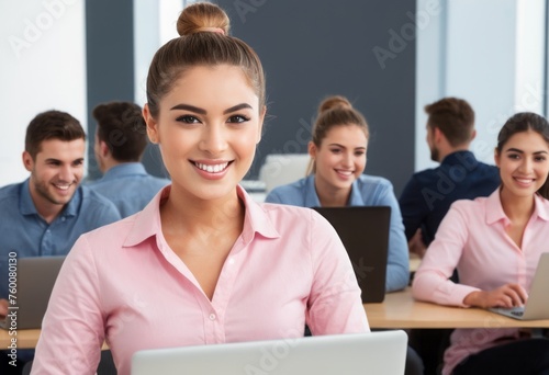 Confident professional woman at her desk in a pink shirt. Office setting with peers in background.