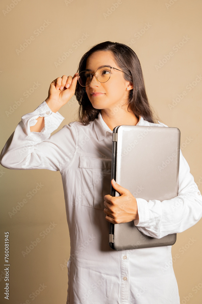 Young happy smiling woman in casual clothes holding a laptop and looking aside holding her glasses. Isolated on orange background. Young happy smiling woman in casual clothes holding a laptop and looking aside holding her glasses. Isolated on orange background.