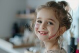 a little smiling girl holds an eyeshadow brush in her hand. The lips are not carefully made up in a childish way with pink lipstick. the girl wants to wear makeup like her mother.