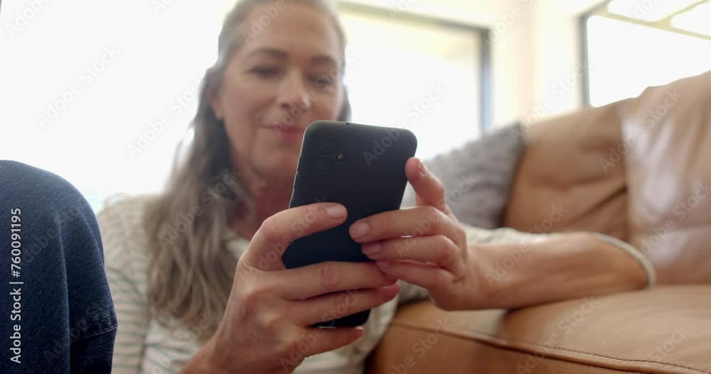 A mature Caucasian woman is smiling at her smartphone on the couch at home A mature Caucasian woman is smiling at her smartphone on the couch at home