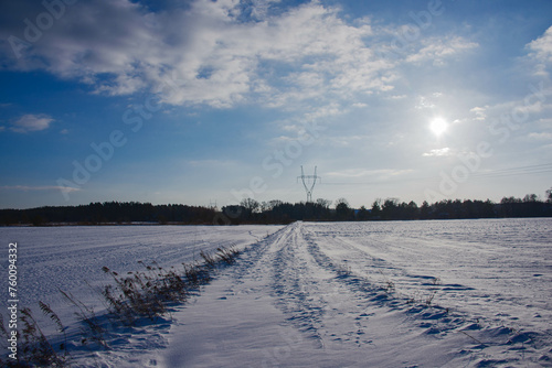 Zimowy, słoneczny dzień. Równina pokryta polami uprawnymi i łąkami pokryta jest warstwą śniegu.