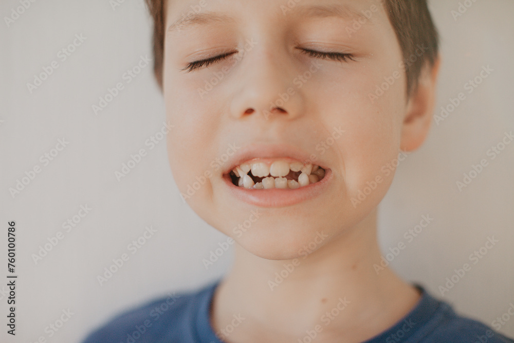 A preschool boy in a blue T-shirt on a light background shows a thumbs up