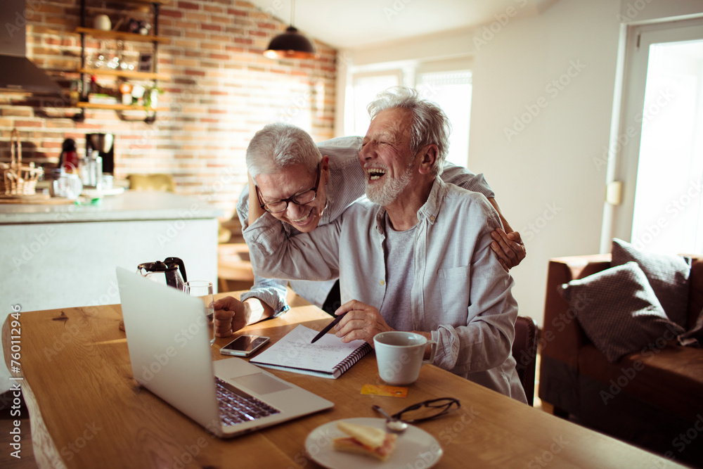 Senior couple laughing and using laptop at home Senior couple laughing and using laptop at home
