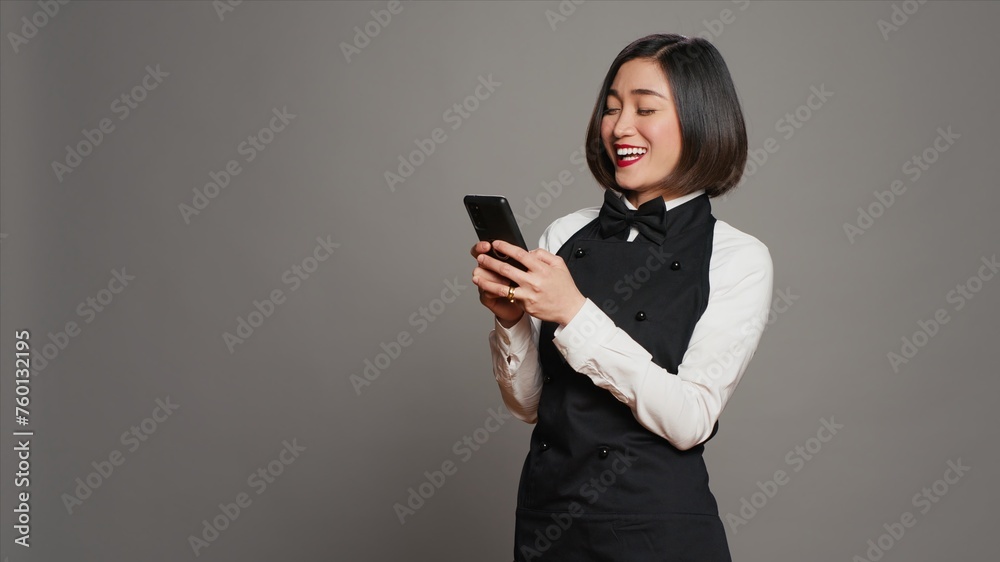 Restaurant hostess texting messages to confirm reservations on phone app, working in catering and serving industry. Asian waitress using smartphone online websites, social media. Camera A. Restaurant hostess texting messages to confirm reservations on phone app, working in catering and serving industry. Asian waitress using smartphone online websites, social media. Camera A.