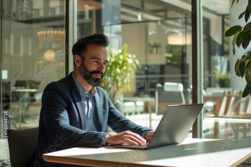 Businessman at work in a sunlit office. A well-groomed businessman working intently on his laptop in a contemporary office environment.