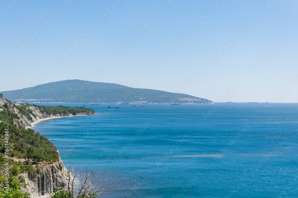 Landscape of the blue sea with a green high coast against the blue sky on a sunny day