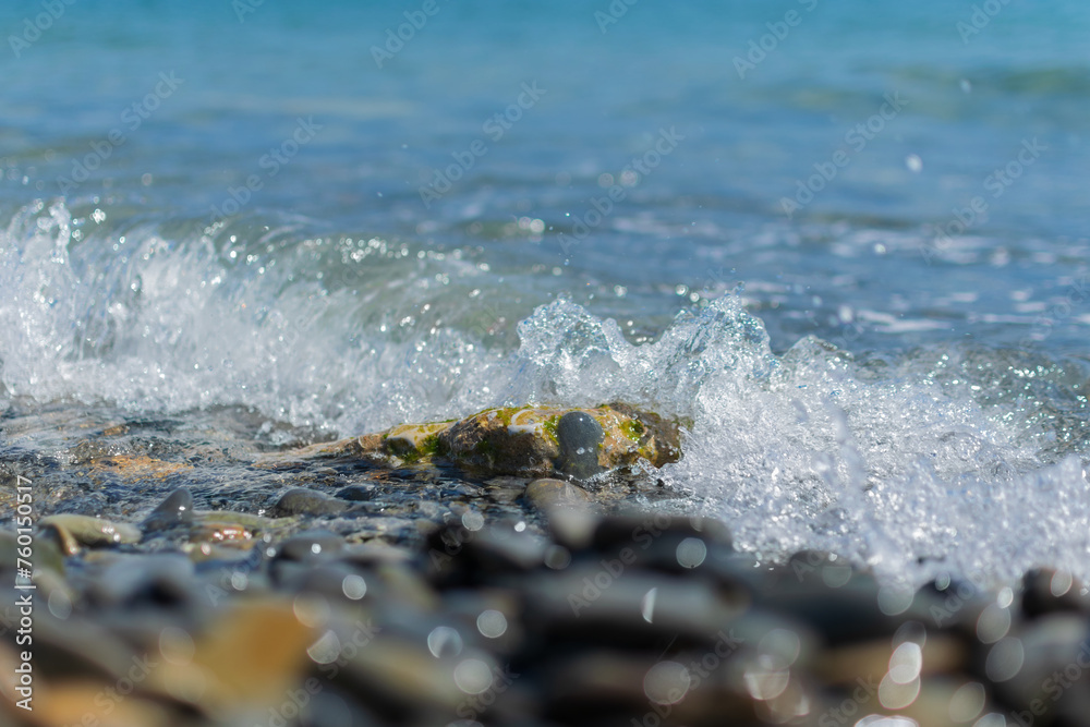 Wet round pebble stones in the foreground are covered by a wave of the blue sea