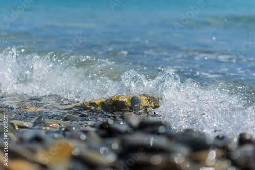 Obraz na płótnie Wet round pebble stones in the foreground are covered by a wave of the blue sea w salonie